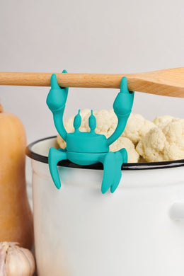 A silicone spoon holder & steam releaser in the shape of a crab and aqua in colour.